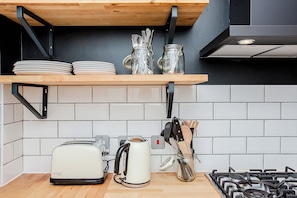 Een keuken met een houten plank waarop borden en potten staan, een broodrooster, een waterkoker en een gasfornuis.