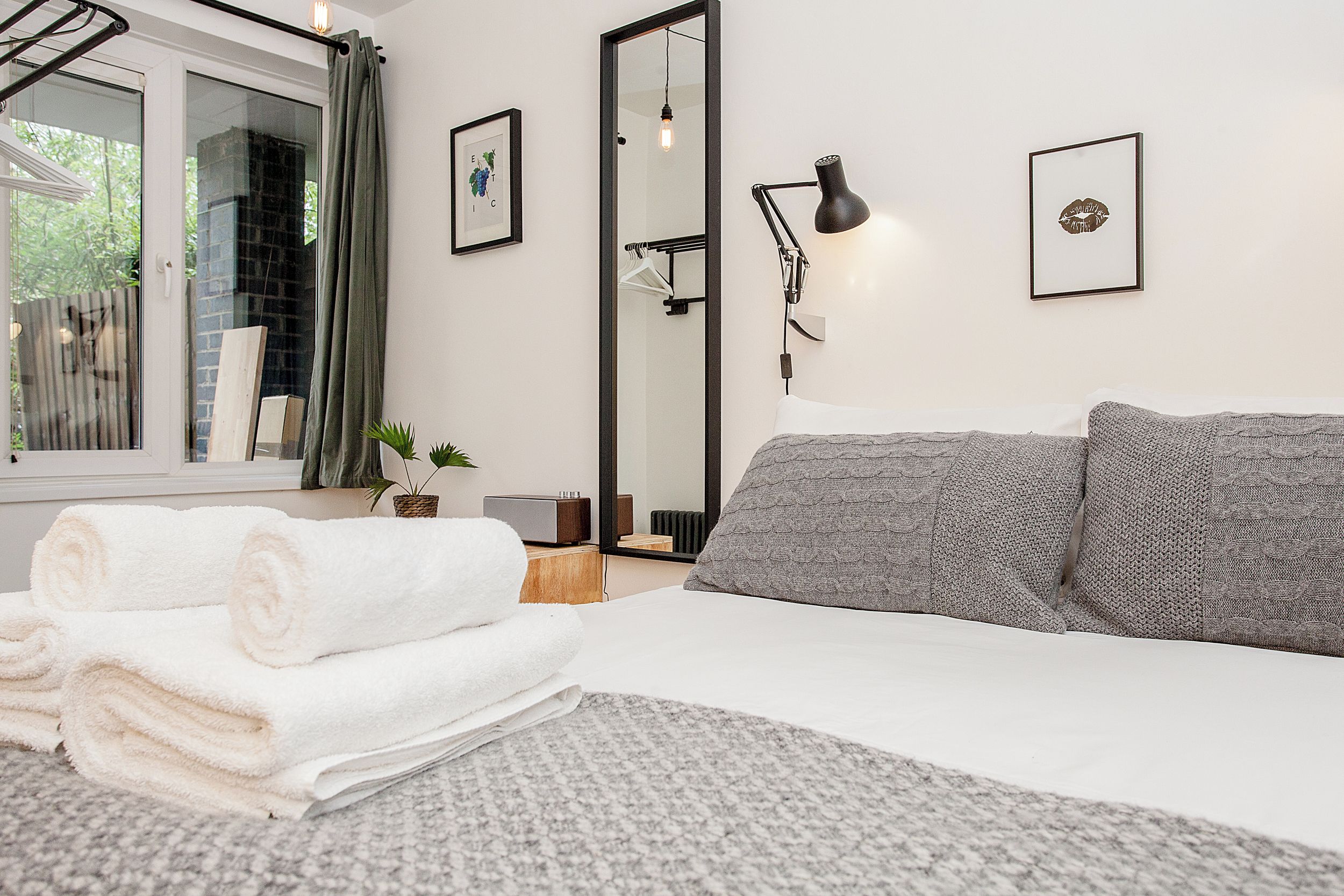 A modern bedroom with a bed, a mirror, a bedside table, and a window with curtains.
