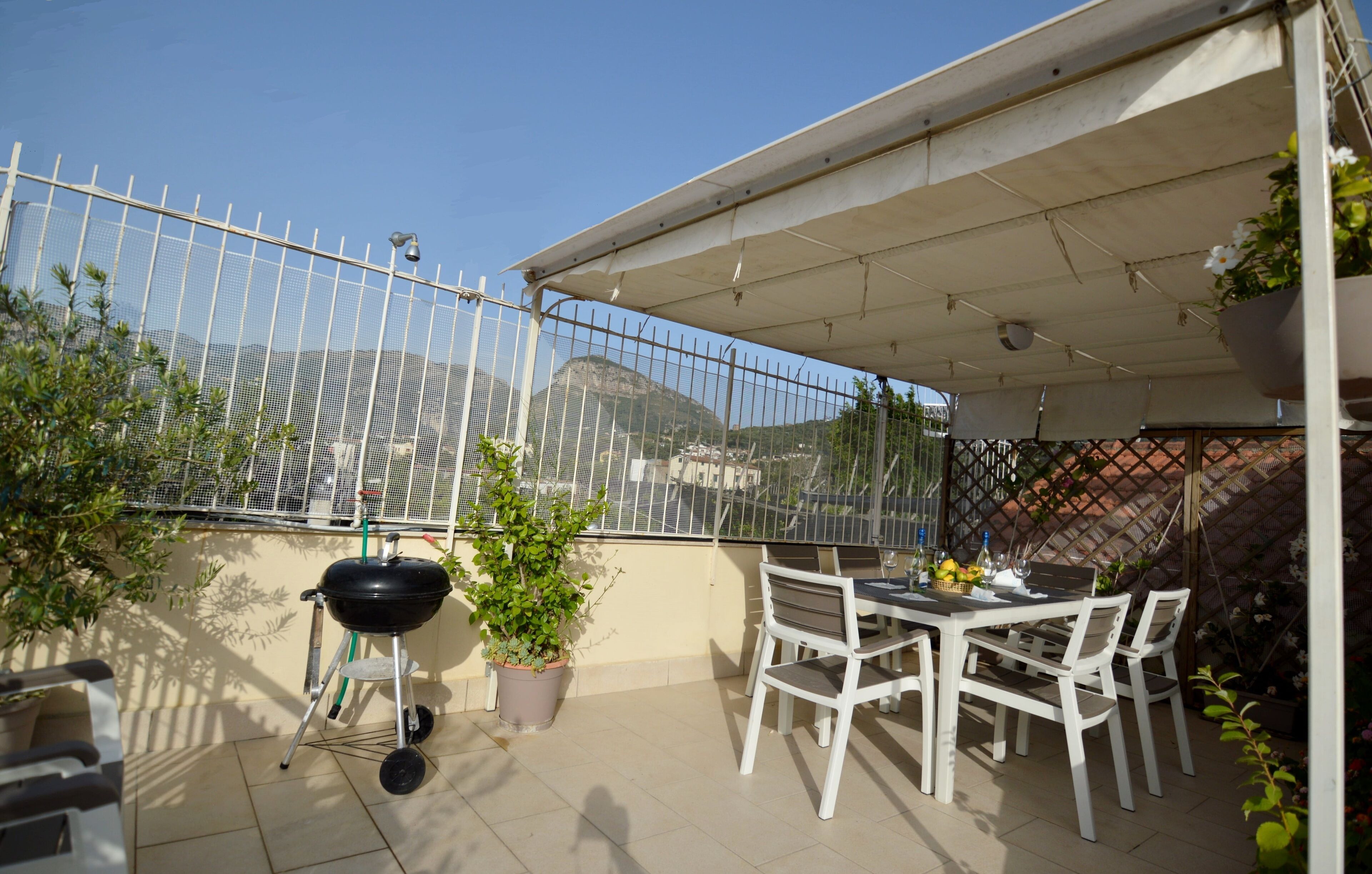 An outdoor patio with a table and chairs, a grill, potted plants, and a view of a mountain.