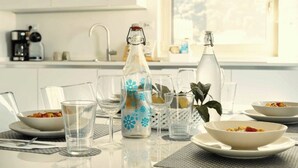 Une table à manger avec de la vaisselle transparente, une bouteille décorative et des bols remplis de nourriture.