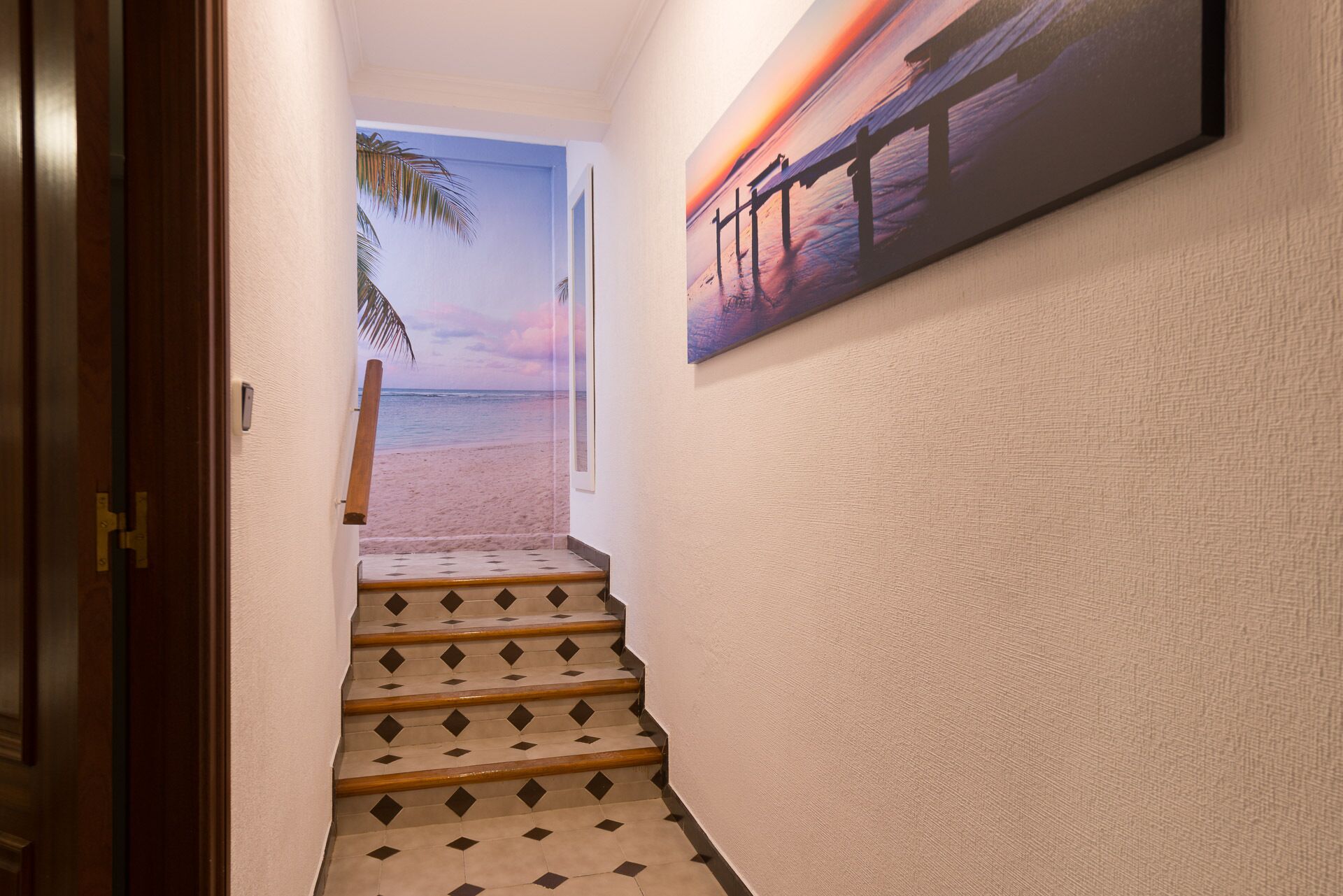 A staircase leading to a beach view with a sunset painting on the wall.