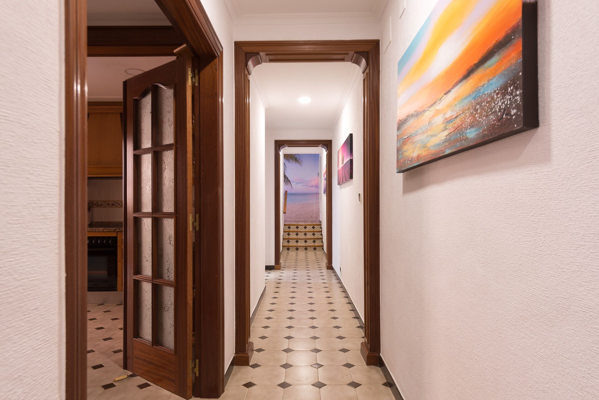 Un pasillo con piso de baldosas, una puerta de madera y un cuadro en la pared.