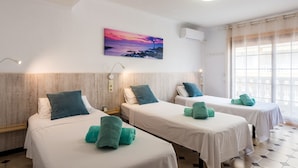 A hotel room with two beds, each with a white bedspread and teal towels. There is a painting of a sunset on the wall, and an air conditioning unit is mounted above the beds. - Beautiful apartment in front of the beach (El campello)
