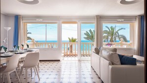 Un salon lumineux avec vue sur la mer, un coin repas avec des chaises et une table, et un canapé agrémenté de coussins.