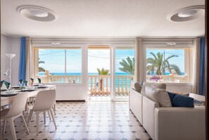 A bright living room with a view of the sea, a dining area with chairs and a table, and a sofa with cushions. - Beautiful apartment in front of the beach (El campello)