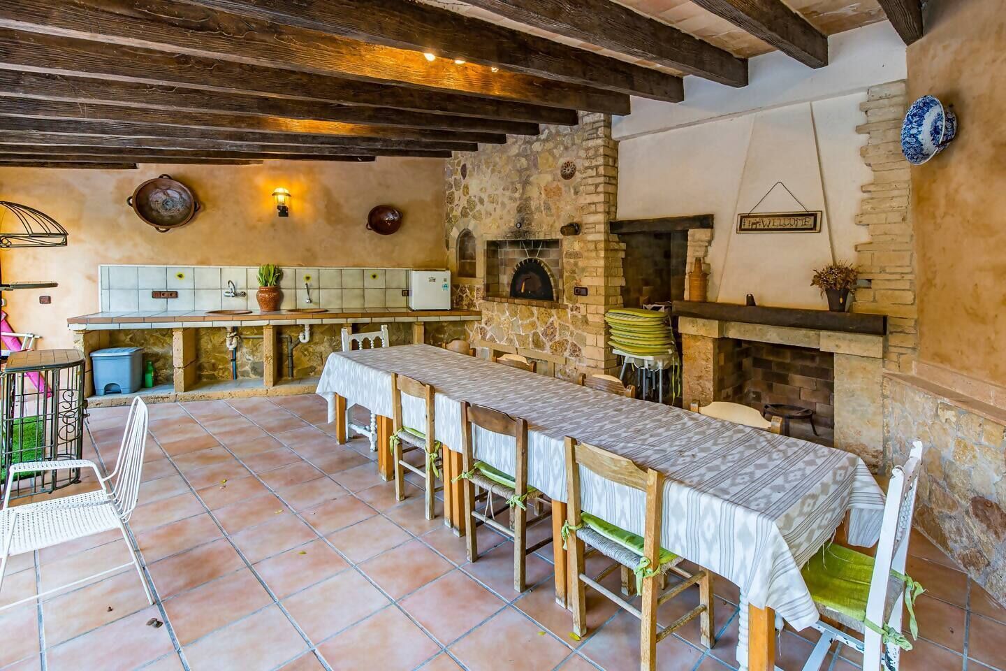 A rustic kitchen with a long wooden table, stone walls, and a stone fireplace.