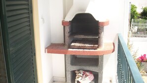 Un petit barbecue d’extérieur fixé à un balcon doté d’une rambarde en métal et d’un mur blanc en arrière-plan.