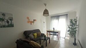 Un salon comprenant un canapé, une table basse, une table à manger avec des chaises, un luminaire suspendu et une plante en pot.