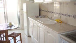 Une cuisine avec des armoires blanches, un évier et une cuisinière. Il y a une fenêtre qui donne sur l’extérieur.