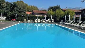 A clear blue swimming pool with lounge chairs and umbrellas, surrounded by trees and buildings.
