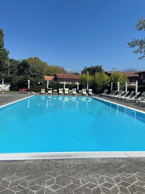 A clear blue swimming pool with lounge chairs and umbrellas, surrounded by trees and buildings. - VerdeCielo in Marina di Massa, Eliana's cottage (Marina di Massa)