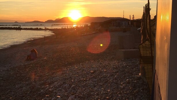 A beach scene with a sunset, pebbles, and a pier in the background. - VerdeCielo in Marina di Massa, Eliana's cottage  (Marina di Massa)