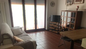 A living room with a sofa, a small round table, a TV on a stand, a wooden cabinet, and a dining table with chairs. - VerdeCielo in Marina di Massa, Eliana's cottage  (Marina di Massa)