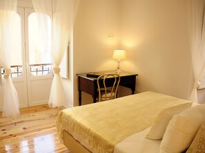 A bedroom with a bed, a desk with a lamp, and a chair.