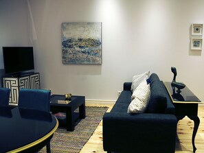 A modern living room with a dark blue sofa, a black coffee table, and a flat-screen TV on a cabinet. - Elegant apartment in downtown Setúbal with air conditioning (Setúbal)