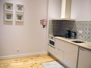 A kitchen with white cabinets, a stove, a sink, and a coffee maker. There are four framed tiles on the wall and a small rug on the floor.