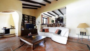 Un soggiorno con un divano bianco, un tavolino in legno, una televisione e una libreria.