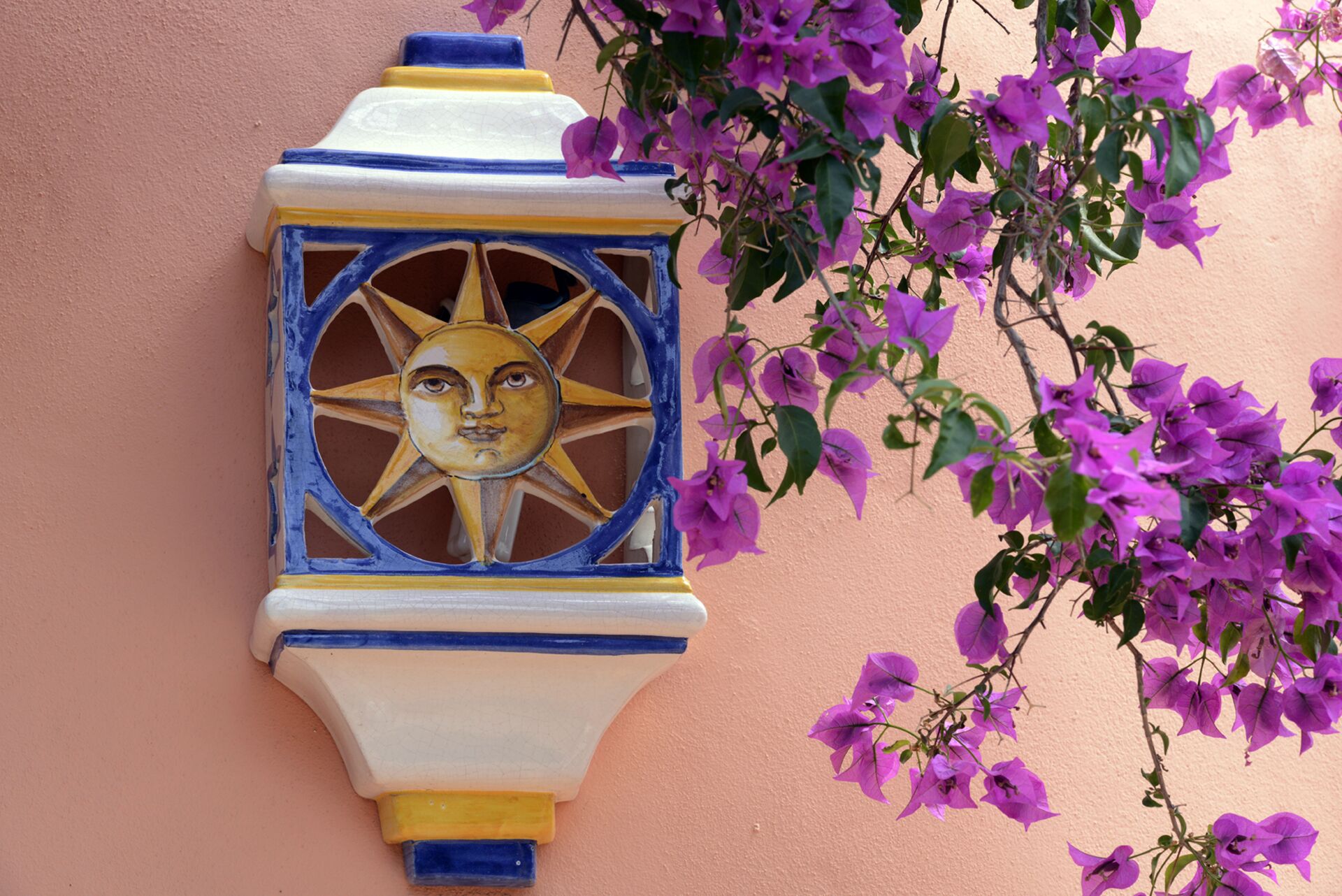 A wall-mounted decorative object with a sun motif, surrounded by purple flowers.