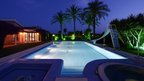 Una piscina con uno scivolo, palme e un edificio illuminato.