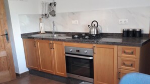 A kitchen with wooden cabinets, a gas stove, and a microwave. There is a rug on the floor and a glass table in the foreground. - Kayenne 2 ,2 bedroom self catering apartment (Iznajar)