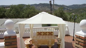 A covered outdoor seating area with a table and chairs, surrounded by brick pillars and white railings, overlooking a vineyard. - Kayenne 2 ,2 bedroom self catering apartment (Iznajar)