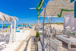 Une terrasse au bord de la plage, dotée de mobilier en bois, d’un toit de chaume et offrant une vue sur la plage.