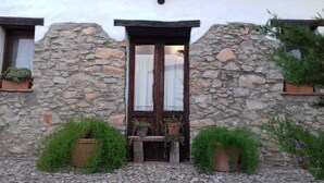 Une façade en pierre avec une porte en bois, des plantes en pot et un chemin pavé.