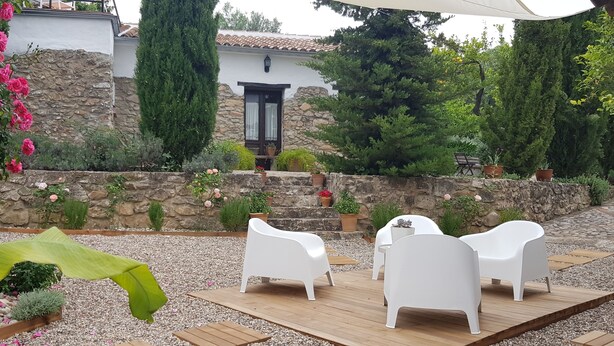 Une terrasse extérieure avec des chaises blanches et une table, entourée d’un mur de pierre et de verdure.
