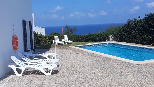 A poolside area with lounge chairs, a lifebuoy, and a clear view of the sea. - House in Calan Morell with garden, private pool and BBQ 300 m from the beach (ciudadela de menorca cALAN morell)