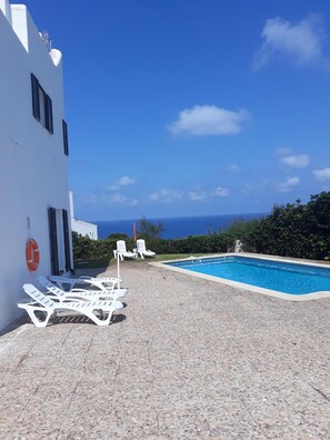 A poolside area with lounge chairs, a lifebuoy, and a clear view of the sea. - House in Calan Morell with garden, private pool and BBQ 300 m from the beach (ciudadela de menorca cALAN morell)
