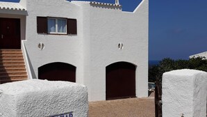 A white building with a staircase leading to a door, a window, and a door with a number plaque. - House in Calan Morell with garden, private pool and BBQ 300 m from the beach (ciudadela de menorca cALAN morell)