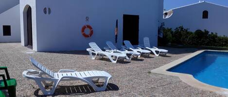 Zona de piscina con sillones blancos y una alberca.