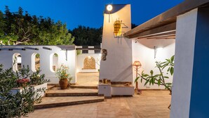 Un patio con zona de estar central, pared de piedra y plantas en macetas.