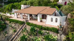 Una villa blanca con techo de tejas, un patio con mobiliario exterior y una escalera que lleva a la entrada.