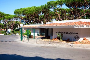 Un edificio con un cartello che recita 'aldeia das acoletas' e un'area salotto esterna recintata, con tavoli e sedie.