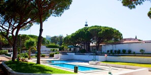 A pool area with a clear sky, surrounded by trees and a white building with a red roof.