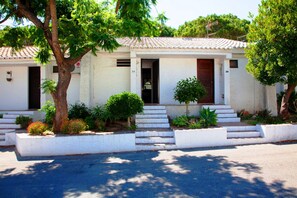 A two-story building with a tiled roof, numbered doors, and a small garden with steps leading to the entrance.