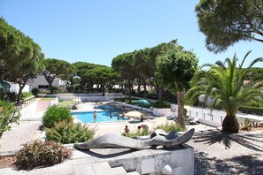 A swimming pool area with a stone sculpture, surrounded by trees and a paved walkway.