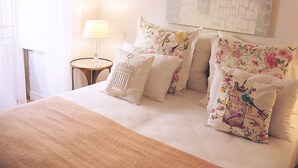A neatly made bed with floral pillows, a bedside lamp, and a wall art piece. - Fully equipped air-conditioned apartment in central Setúbal (Setúbal)