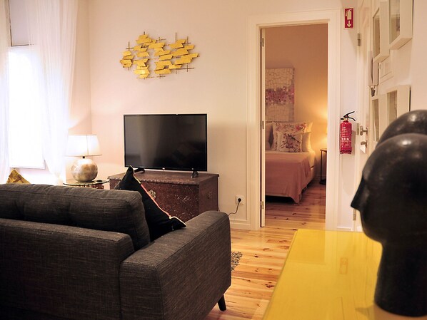 A living room with a flat-screen TV, a sofa, a lamp, and a decorative wall piece.