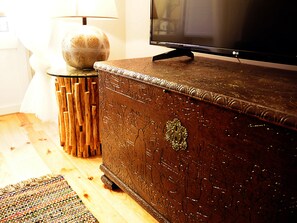 A wooden chest with intricate carvings, a television on a stand, and a lamp beside it.
