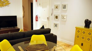 A living room with a gray sofa, yellow chairs, a glass table, a TV, and a yellow cabinet. - Fully equipped air-conditioned apartment in central Setúbal (Setúbal)