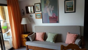 A room with a striped sofa, a wooden chair, a lamp, and several framed pictures on the wall. - APARTMENT NEXT TO THE SEA WITH COMMUNITY GARDEN AND PLAZA PARKING WITH FREE WIFI (Platja d'Aro)