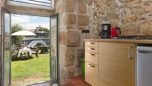 Cocina con paredes de piedra, encimera de madera, cafetera y vistas a un jardín con mesa y sillas.