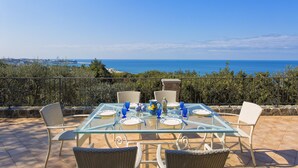 A glass-top table set for dining with wicker chairs, overlooking a coastal view. - Luxury villa with panoramic swimming pool in Ischia, near Amalfi Coast (Forio)