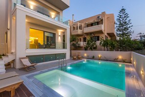 A modern poolside area with a glass balustrade, lounge chairs, and a clear pool. - Luxury Villa Amelia (Chania)