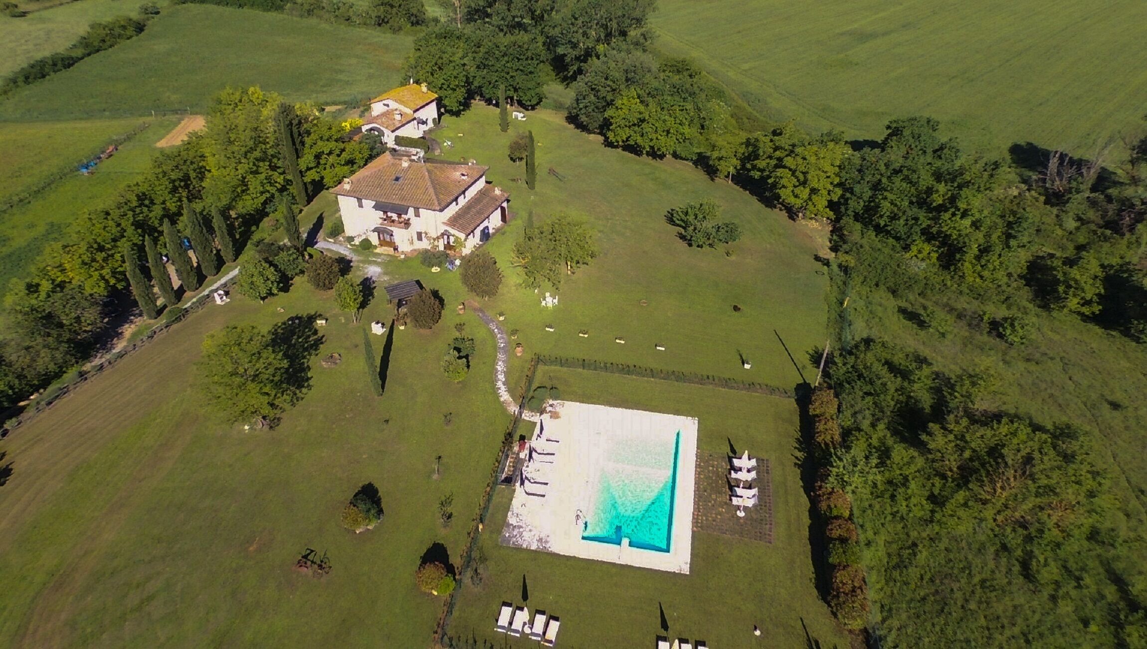 Vista aérea de uma grande propriedade com piscina, vários edifícios e amplos gramados verdes.