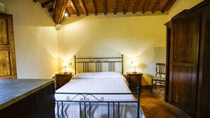 A bedroom with a bed, two bedside tables with lamps, a wooden wardrobe, and a wooden chair. - CHARMING APARTMENT WITH POOL - 40 KM FLORENCE, 20 KM SIENA, 15 KM S. GIMIGNANO (Monteriggioni)
