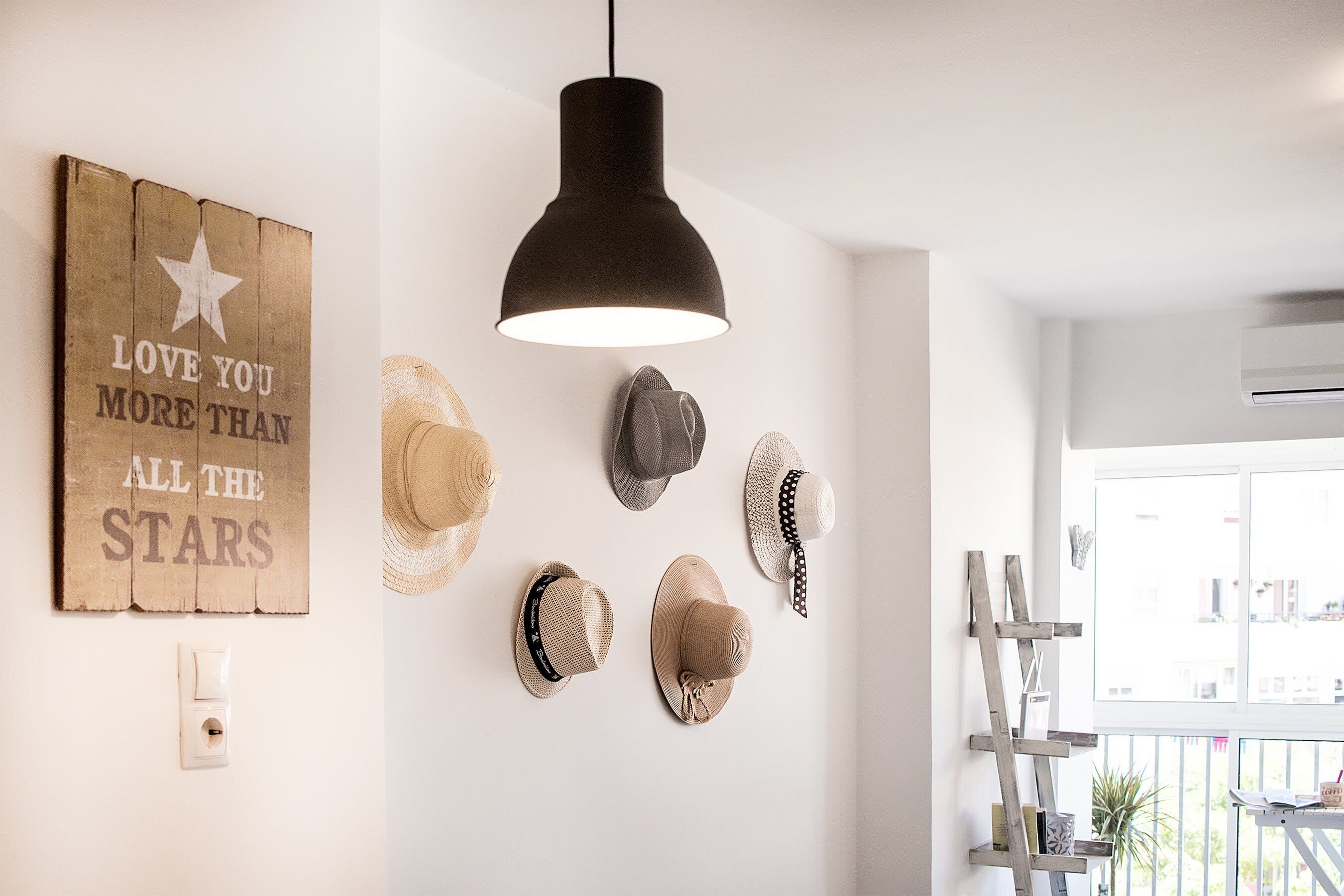 A room with a wooden wall decoration, a black pendant light, and several hats hanging on the wall.