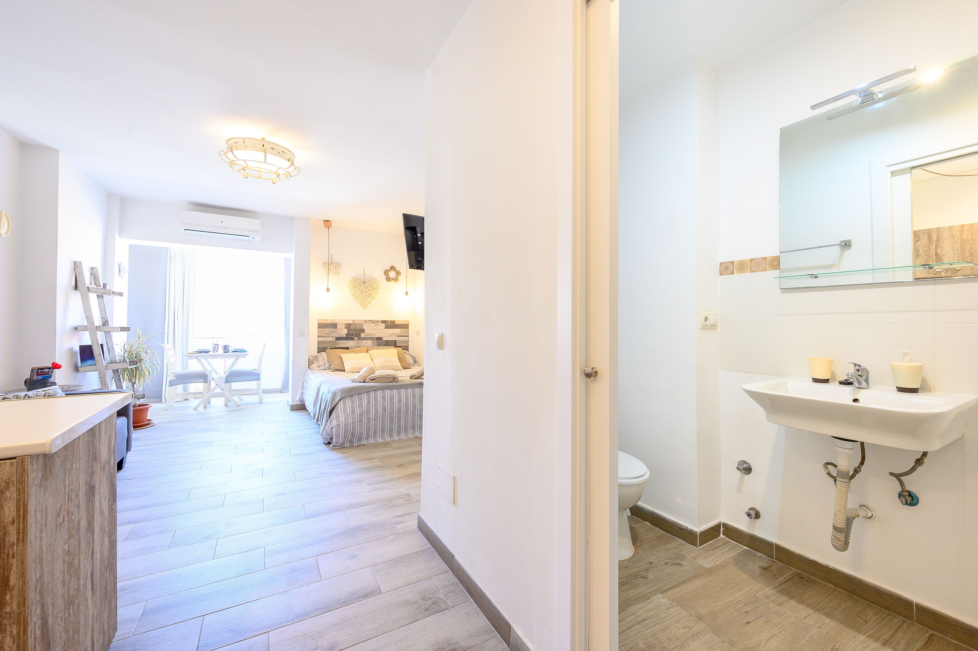 Une salle de bain moderne avec un lavabo blanc, un miroir et des toilettes. Un couloir mène à un coin repas équipé d’une table et de chaises.